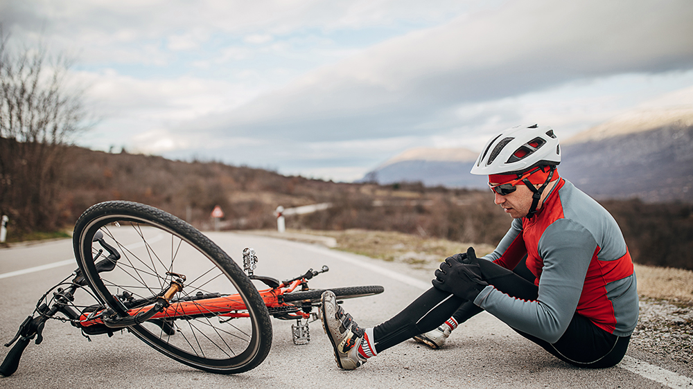 Cycling holding knee on ground next to bike