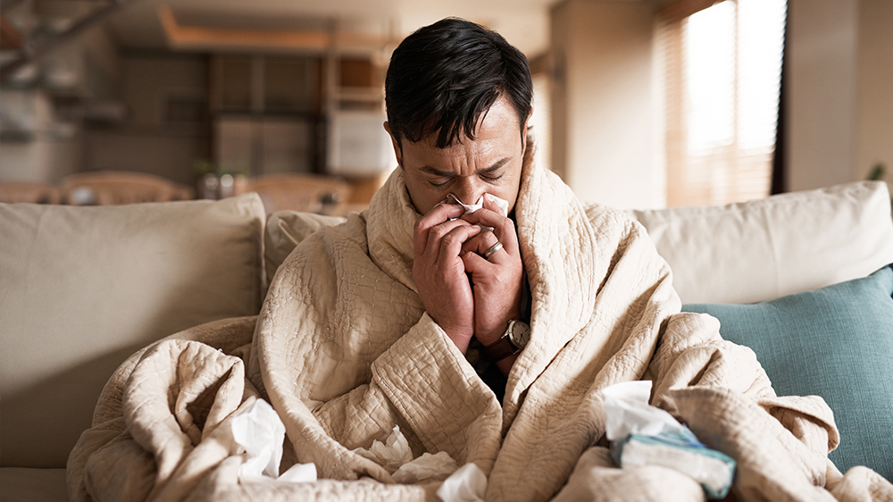 Sick man with facial tissue blowing nose